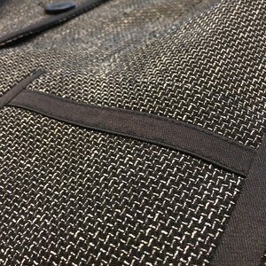 Puede incluir: Primer plano de una chaqueta negra con tejido texturizado. La chaqueta tiene un ribete negro y un bolsillo en la parte delantera.