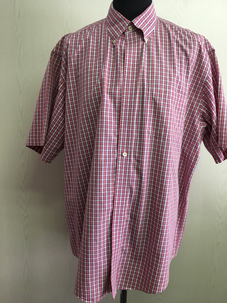 Pu&ograve; includere: Una camicia a maniche corte con bottoni a quadri rossi e bianchi.