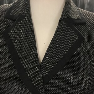 Puede incluir: Una chaqueta negra con un patr&oacute;n texturizado blanco y un ribete negro alrededor del cuello.