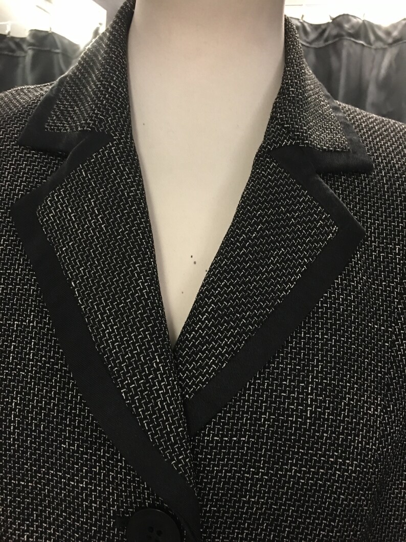 Puede incluir: Una chaqueta negra con un patr&oacute;n texturizado blanco y un ribete negro alrededor del cuello.