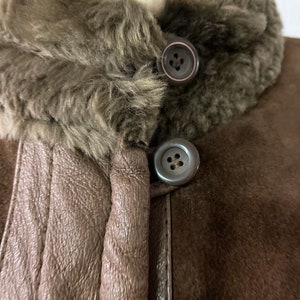 May include: Close-up of a brown suede jacket with a brown faux fur collar. The jacket has two large buttons on the front.