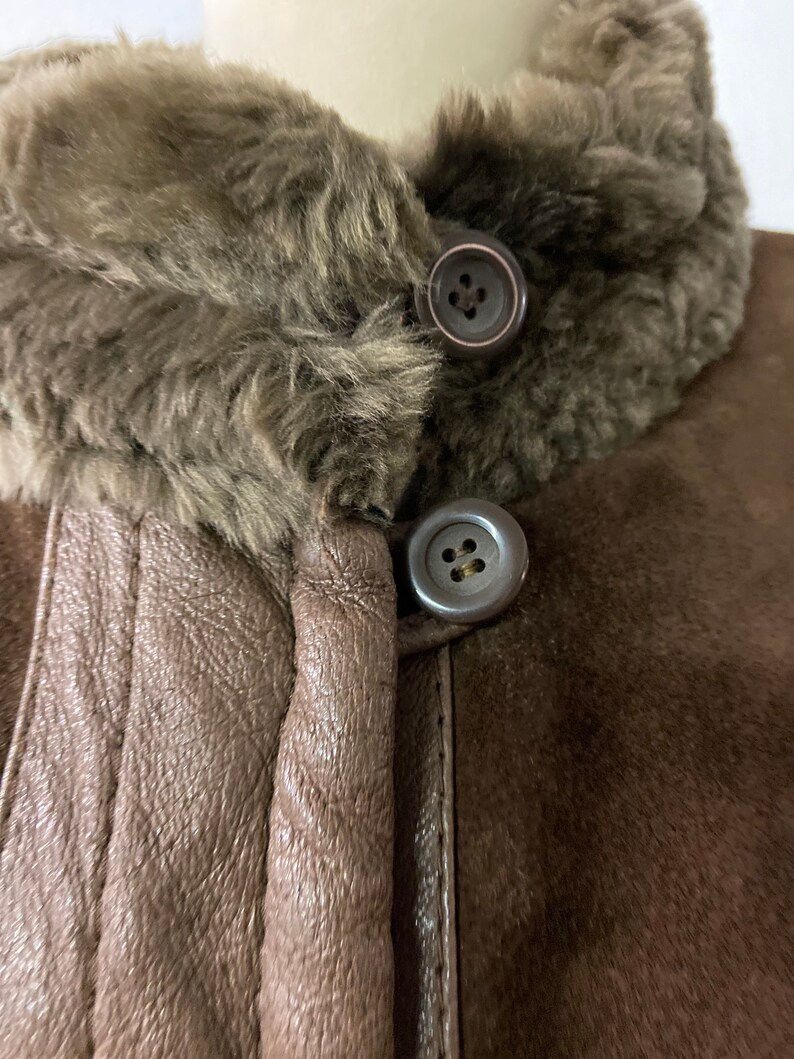 May include: Close-up of a brown suede jacket with a brown faux fur collar. The jacket has two large buttons on the front.