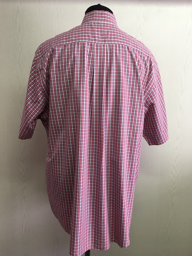 Pu&ograve; includere: Una camicia a maniche corte con bottoni a quadri rossi e bianchi.
