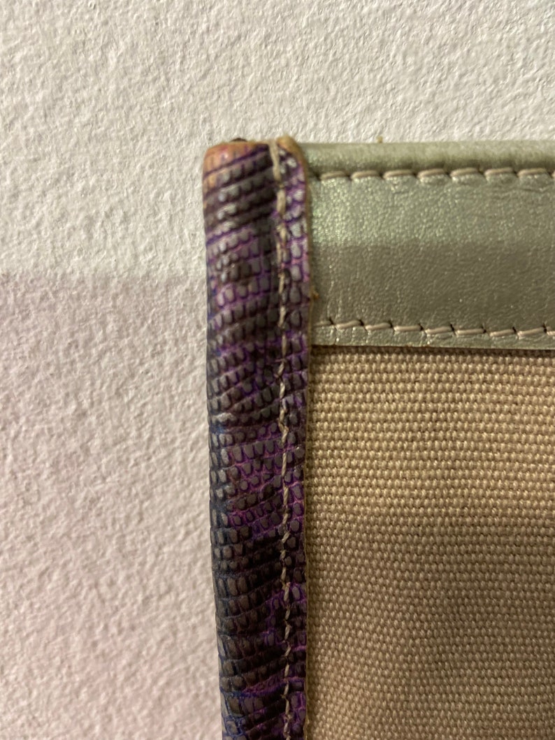 May include: Close-up of the edge of a beige canvas bag with a purple leather trim. The leather trim has a textured, scaly pattern.
