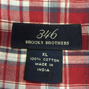 Puede incluir: Una camisa de cuadros rojos y blancos con una etiqueta azul que dice "346 Brooks Brothers" y "XL 100% Algod&oacute;n Hecho en India".