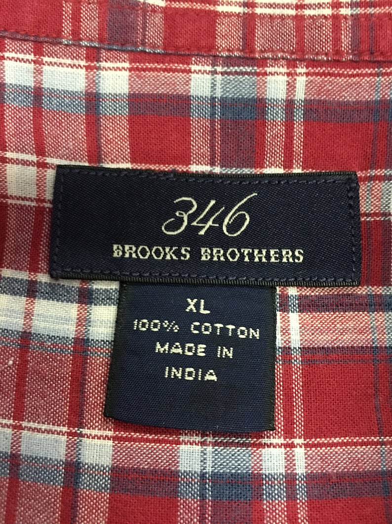 Puede incluir: Una camisa de cuadros rojos y blancos con una etiqueta azul que dice "346 Brooks Brothers" y "XL 100% Algod&oacute;n Hecho en India".