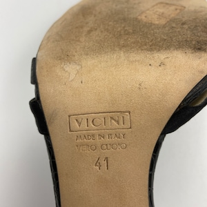 May include: Close-up of the bottom of a black leather sandal with a brown leather sole. The sole is labeled "Vicini Made in Italy Vero Cuoio 41".