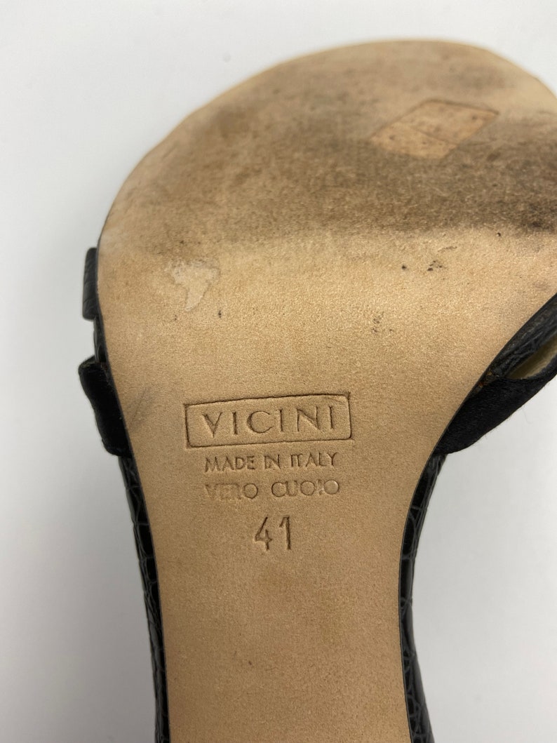 May include: Close-up of the bottom of a black leather sandal with a brown leather sole. The sole is labeled "Vicini Made in Italy Vero Cuoio 41".