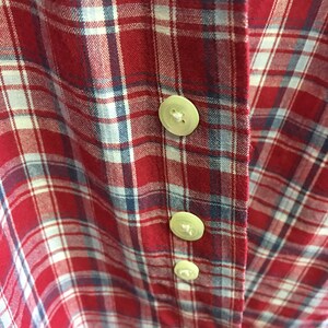 Puede incluir: Camisa de cuadros rojos, blancos y azules con tres botones blancos. Los botones est&aacute;n cosidos en el lado derecho de la camisa.