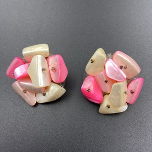 May include: A pair of pink and white clip-on earrings made of plastic. The earrings are shaped like clusters of small, irregular stones.