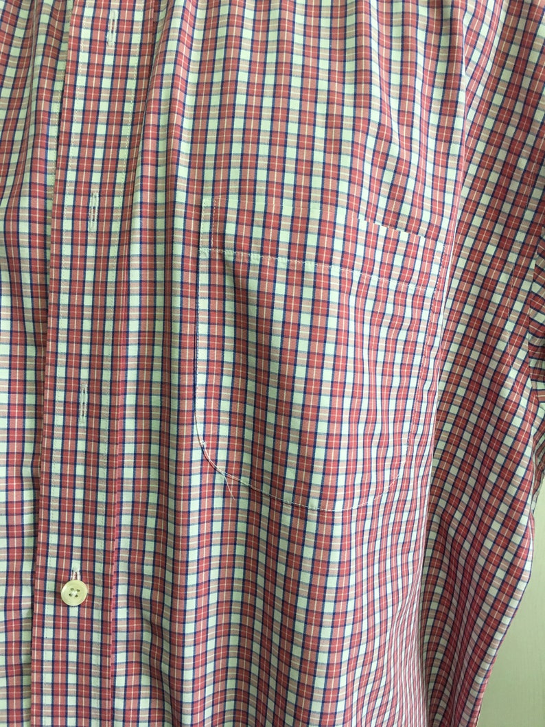 Pu&ograve; includere: Una camicia a bottoni a quadri rossi e bianchi con una chiusura a bottone singolo e una tasca sul lato sinistro.