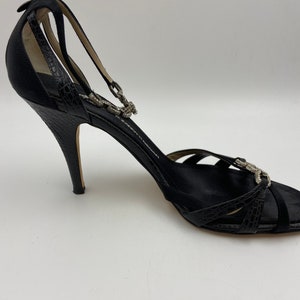 May include: Black satin heeled sandals with a rhinestone ankle strap and a peep toe.