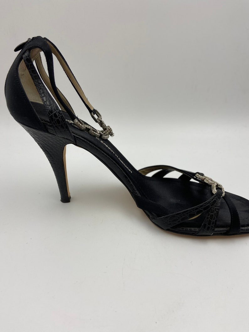 May include: Black satin heeled sandals with a rhinestone ankle strap and a peep toe.