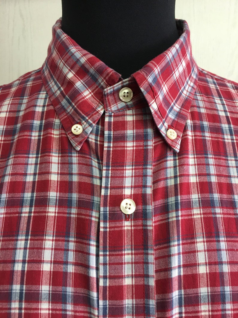 Puede incluir: Una camisa de botones a cuadros rojos y blancos con detalles azules.