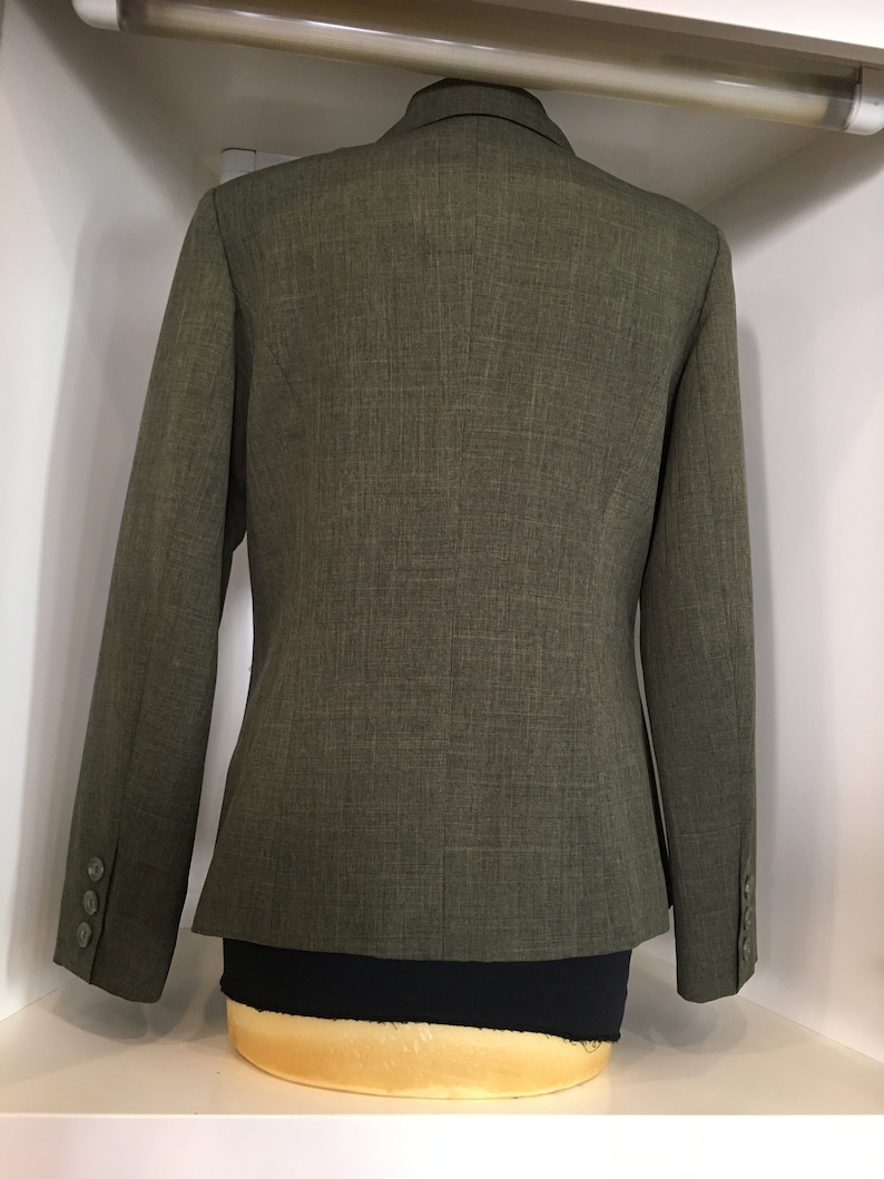 Op de afbeelding: Een groene blazer van een getextureerde stof. De blazer heeft een enkele knoopsluiting en lange mouwen.