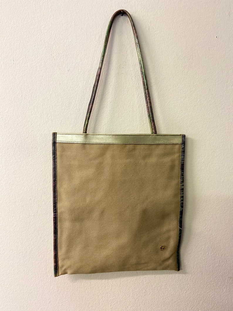 May include: A beige canvas tote bag with a gold trim and green and purple patterned straps.