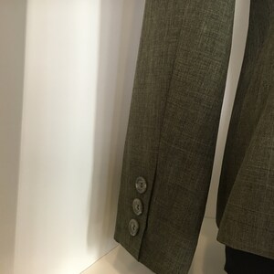 Op de afbeelding: Een donkergroen blazer met drie knopen op de manchet van de mouw.