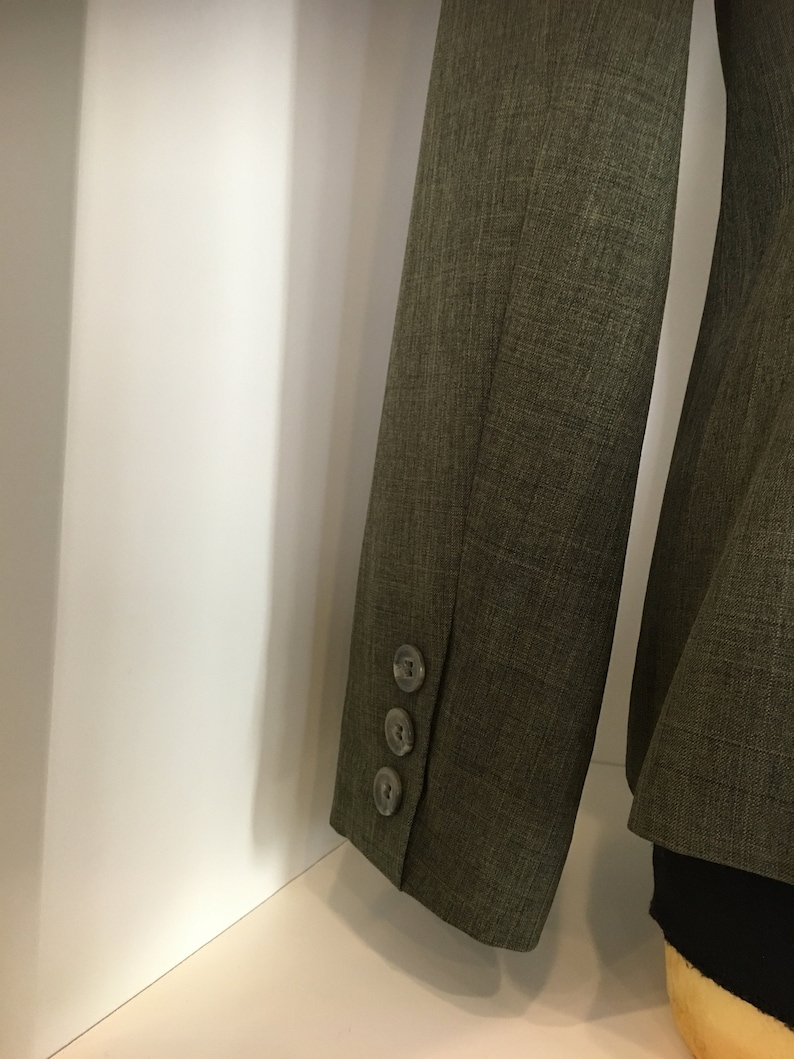 Op de afbeelding: Een donkergroen blazer met drie knopen op de manchet van de mouw.