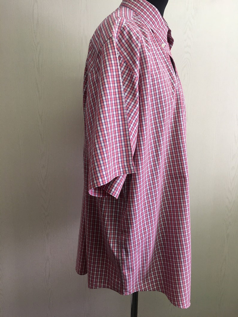 Pu&ograve; includere: Una camicia a maniche corte con bottoni a quadri rossi e bianchi.