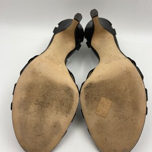 May include: A pair of black leather heeled sandals with a buckle strap. The sandals have the text "VALENTINO GARAVANI" and "37" printed on the soles.