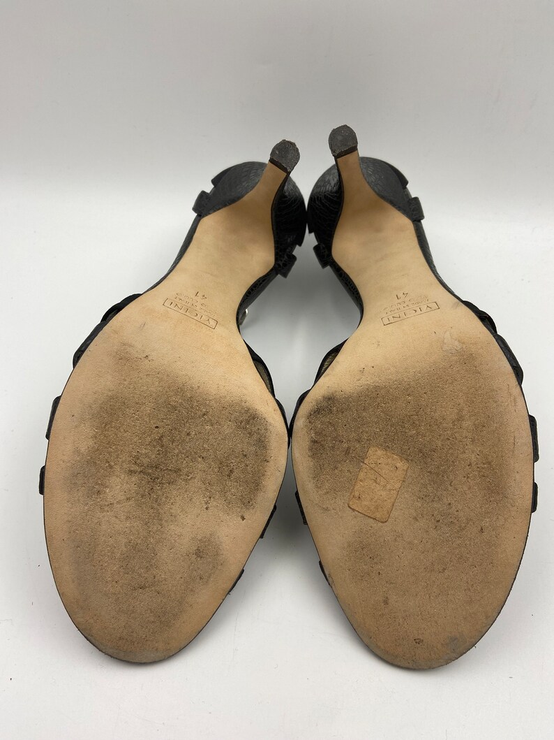 May include: A pair of black leather heeled sandals with a buckle strap. The sandals have the text "VALENTINO GARAVANI" and "37" printed on the soles.