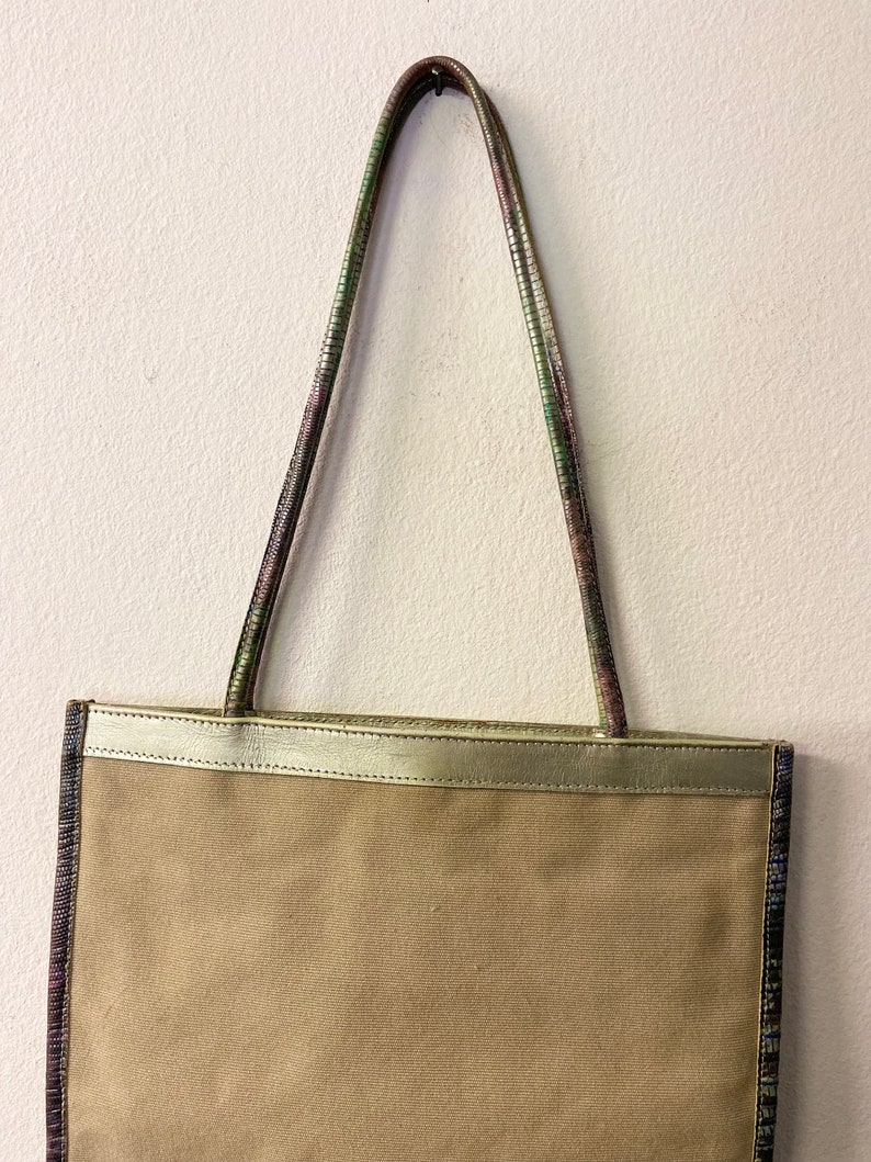 May include: A beige canvas tote bag with a gold leather trim and multi-coloured patterned straps.
