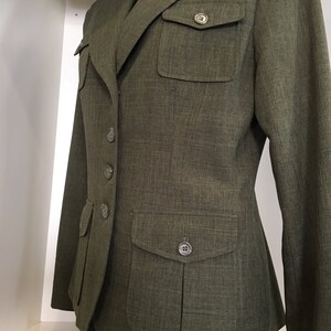 Op de afbeelding: Een groene blazer met knoopsluiting en twee klepzakken. De blazer heeft een textuur in de stof en een aansluitende pasvorm.