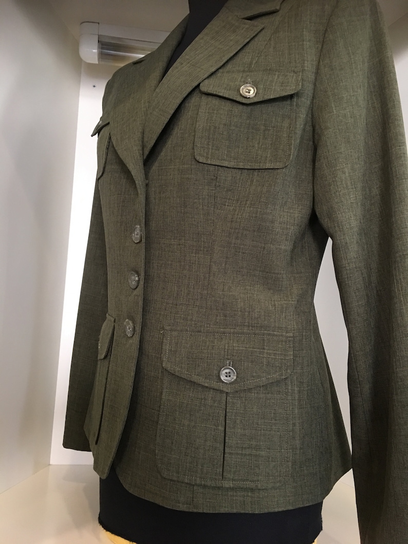 Op de afbeelding: Een groene blazer met knoopsluiting en twee klepzakken. De blazer heeft een textuur in de stof en een aansluitende pasvorm.