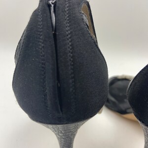 May include: A pair of black high-heeled shoes with a zipper on the back. The heels are a snakeskin pattern.