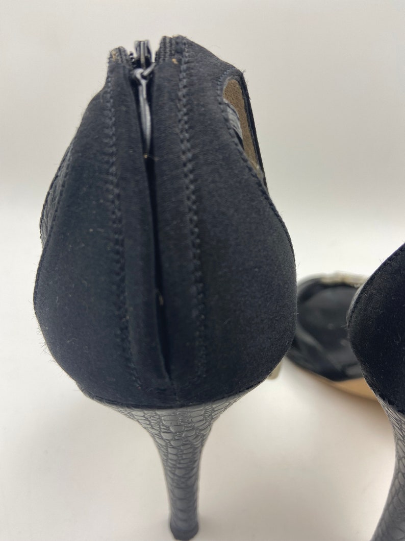 May include: A pair of black high-heeled shoes with a zipper on the back. The heels are a snakeskin pattern.