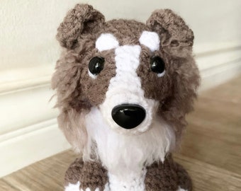 May include: A crocheted stuffed dog toy with brown and white fur. The dog has black eyes and a black nose.