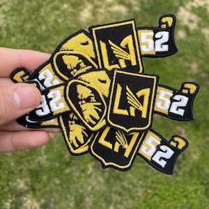 May include: Four black and gold embroidered patches with the letter "L" and the number "52" on them.