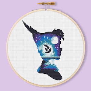 May include: A cross-stitch embroidery hoop featuring a silhouette of Peter Pan, the Disney character, with a starry night sky and moon inside the silhouette.