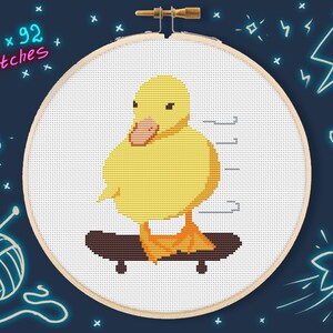 May include: A yellow duckling cross-stitched pattern on white Aida cloth, riding a brown skateboard. The pattern is framed in a wooden embroidery hoop. The text "72 x 92 stitches" is written in pink on a black background.