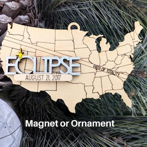 May include: Wooden ornament or magnet shaped like the United States with the word "ECLIPSE" and the date "AUGUST 21, 2017" on it. The path of totality is marked on the map.