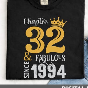 May include: Black t-shirt with a gold crown and the text "Chapter 32 & Fabulous Since 1994". The number 32 is in a large, bold font. The shirt is folded, with a pair of blue jeans visible in the background.