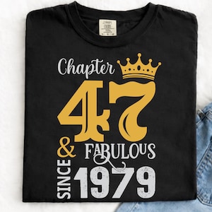 May include: Black t-shirt with a gold crown and the text "Chapter 47 & Fabulous Since 1979". The graphic design is in gold and white. The shirt is paired with blue jeans.