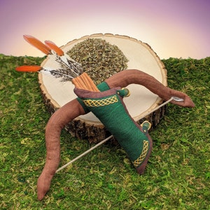May include: A brown leather quiver with a green fabric pouch and gold accents. The quiver is filled with a set of orange and white feathers. The quiver is sitting on a wooden stump.