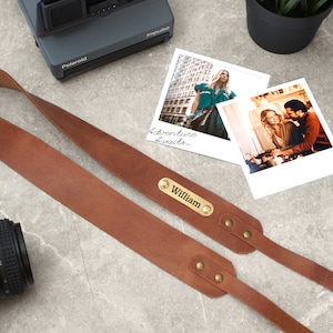 May include: A brown leather camera strap with brass accents and a personalized nameplate that reads "William".