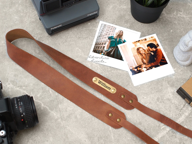 May include: A brown leather camera strap with brass accents and a personalized nameplate that reads "William".