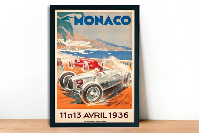 May include: Vintage poster advertising the Monaco Grand Prix, featuring a white and silver race car speeding along a coastal road with a view of the city in the background. The poster is dated "11 et 13 AVRIL 1936" and includes the text "MONACO" in large blue letters.
