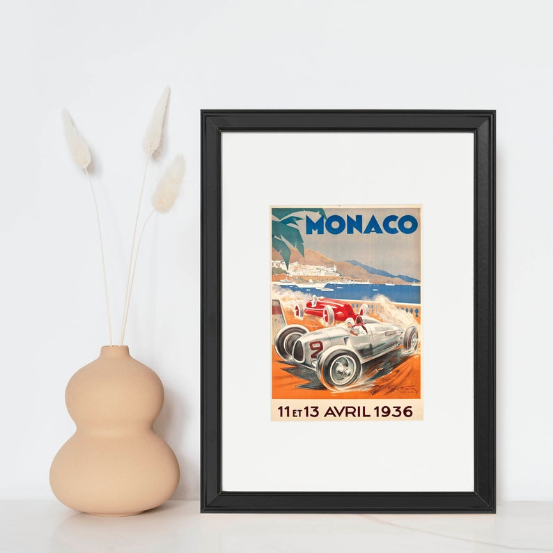 May include: A vintage poster advertising the Monaco Grand Prix, featuring a silver race car with a red car behind it, against a backdrop of a coastal scene. The poster reads "MONACO" and "11 et 13 AVRIL 1936".