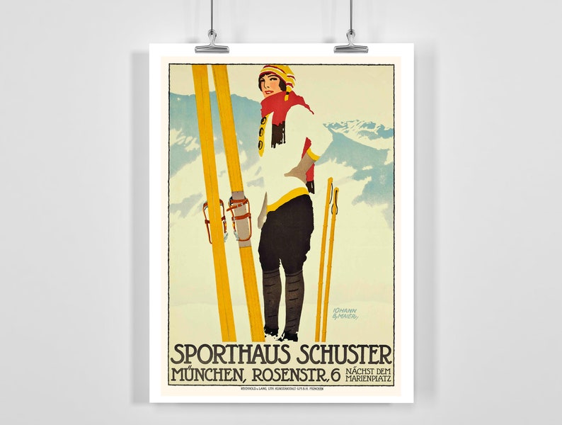 Op de afbeelding: Een vintage skiposter met een vrouw in een wit skipak en rode muts, die ski's en stokken vasthoudt. De poster is in een blauw, wit en geel kleurenschema en bevat de tekst "Sporthaus Schuster M&uuml;nchen, Rosenstr. 6 N&auml;chste dem Marienplatz".