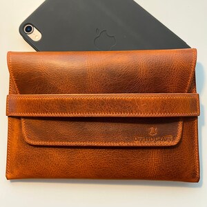 May include: A brown leather iPad case with a flap closure and a strap. The case has a stitched design and the text "OFFITO CRAFT" embossed on the front.