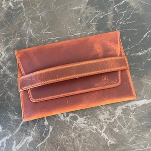 May include: A brown leather wallet with a flap closure and a strap. The wallet has a stitched design and the text "OFFTO CRAFT" embossed on the front.