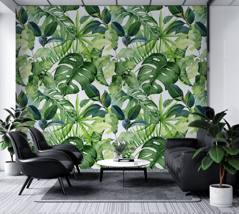 Op de afbeelding: Een woonkamer interieur met een witte muur bedekt met een tropische bladbehang. De kamer heeft twee zwarte stoelen, een zwarte bank en een ronde salontafel.
