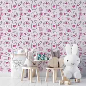 Puede incluir: Papel tapiz de guarder&iacute;a rosa y blanco con un patr&oacute;n repetitivo de art&iacute;culos para beb&eacute;s, que incluyen chupetes, biberones, baberos y patos. El papel tapiz se muestra en una habitaci&oacute;n con un juguete de conejo blanco, una mesa de madera y dos sillas de madera.
