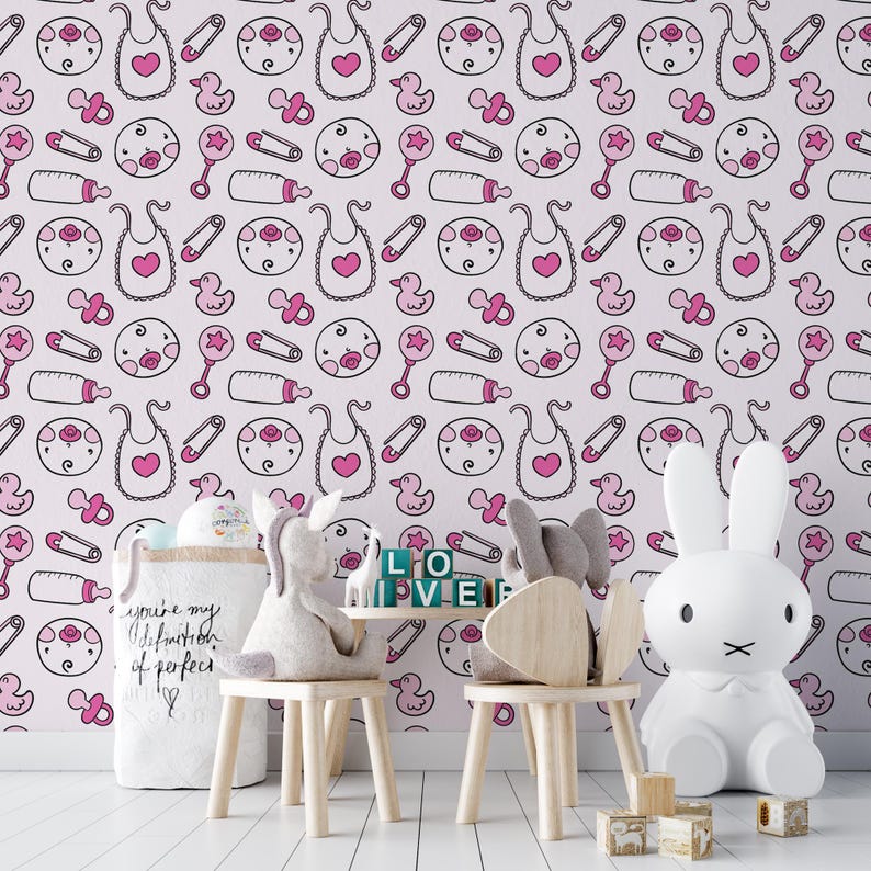 Puede incluir: Papel tapiz de guarder&iacute;a rosa y blanco con un patr&oacute;n repetitivo de art&iacute;culos para beb&eacute;s, que incluyen chupetes, biberones, baberos y patos. El papel tapiz se muestra en una habitaci&oacute;n con un juguete de conejo blanco, una mesa de madera y dos sillas de madera.