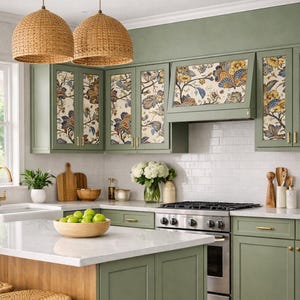 Può includere: Cucina con mobili verde salvia e un'isola con piano di lavoro bianco. La carta da parati floreale adesiva adorna le ante dei mobili. Lampade a sospensione in tessuto sono appese sopra l'isola. Il testo "CABINET MAKEOVER! Peel and Stick Wallpaper" è in alto.