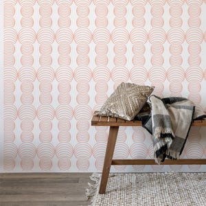 May include: A white wall with a pink geometric pattern wallpaper. A wooden bench with a gold pillow and a black and white throw blanket is in front of the wall.